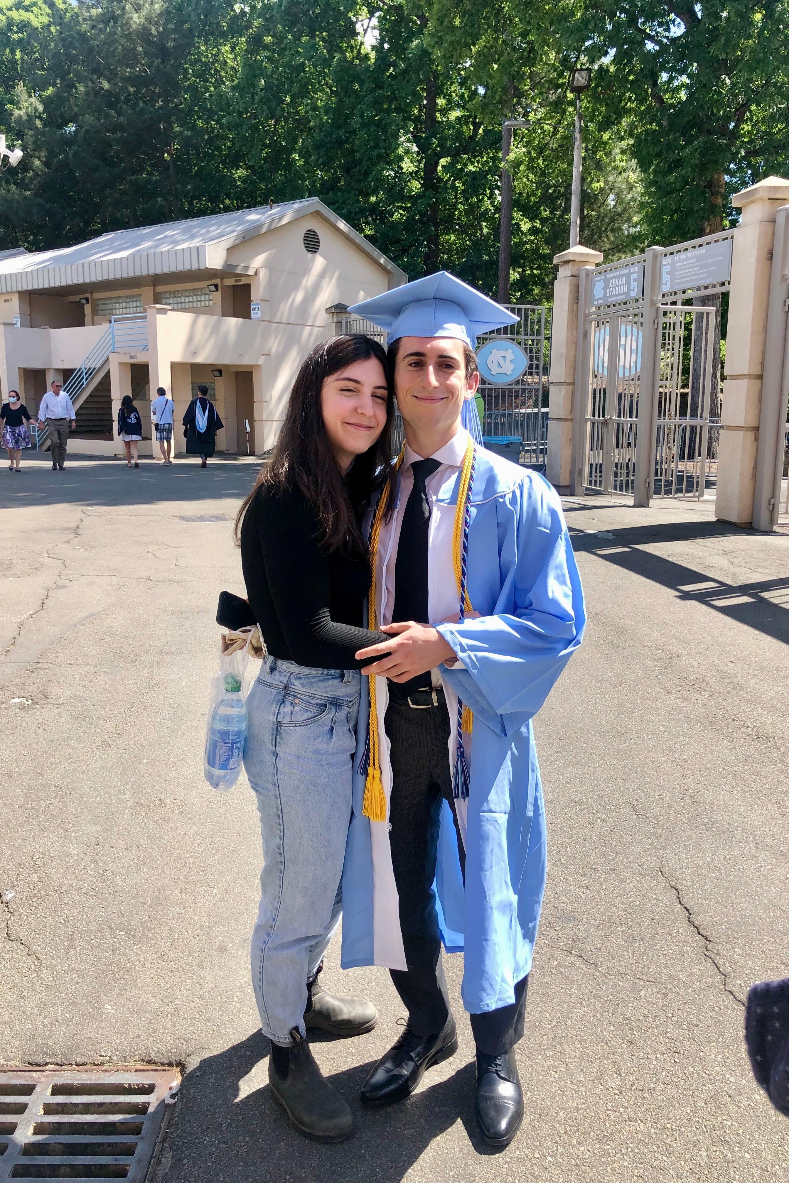 Ari in a Carolina-blue graduation gown, hugging Montana