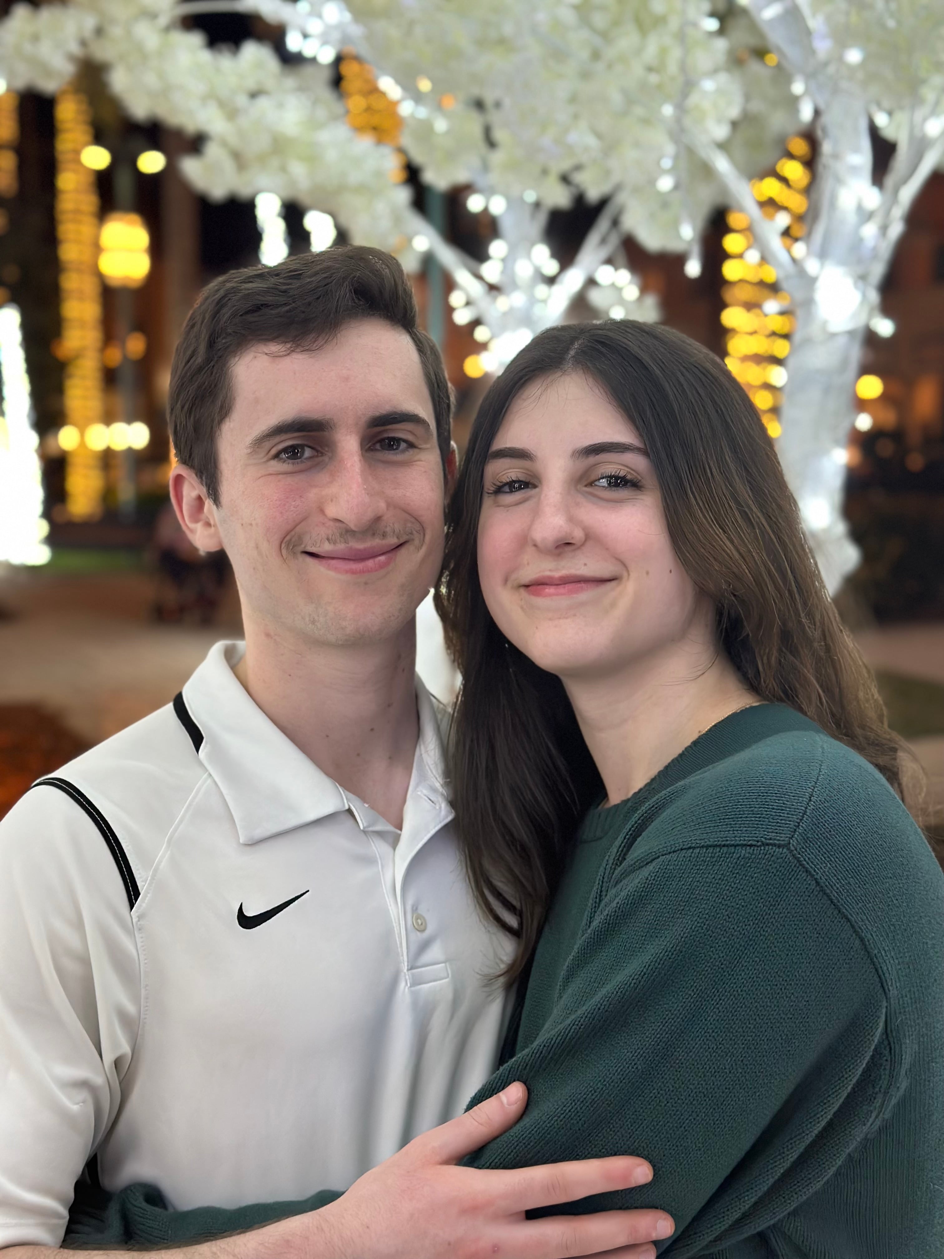 Ari and Montana in front of trees strung with white lights