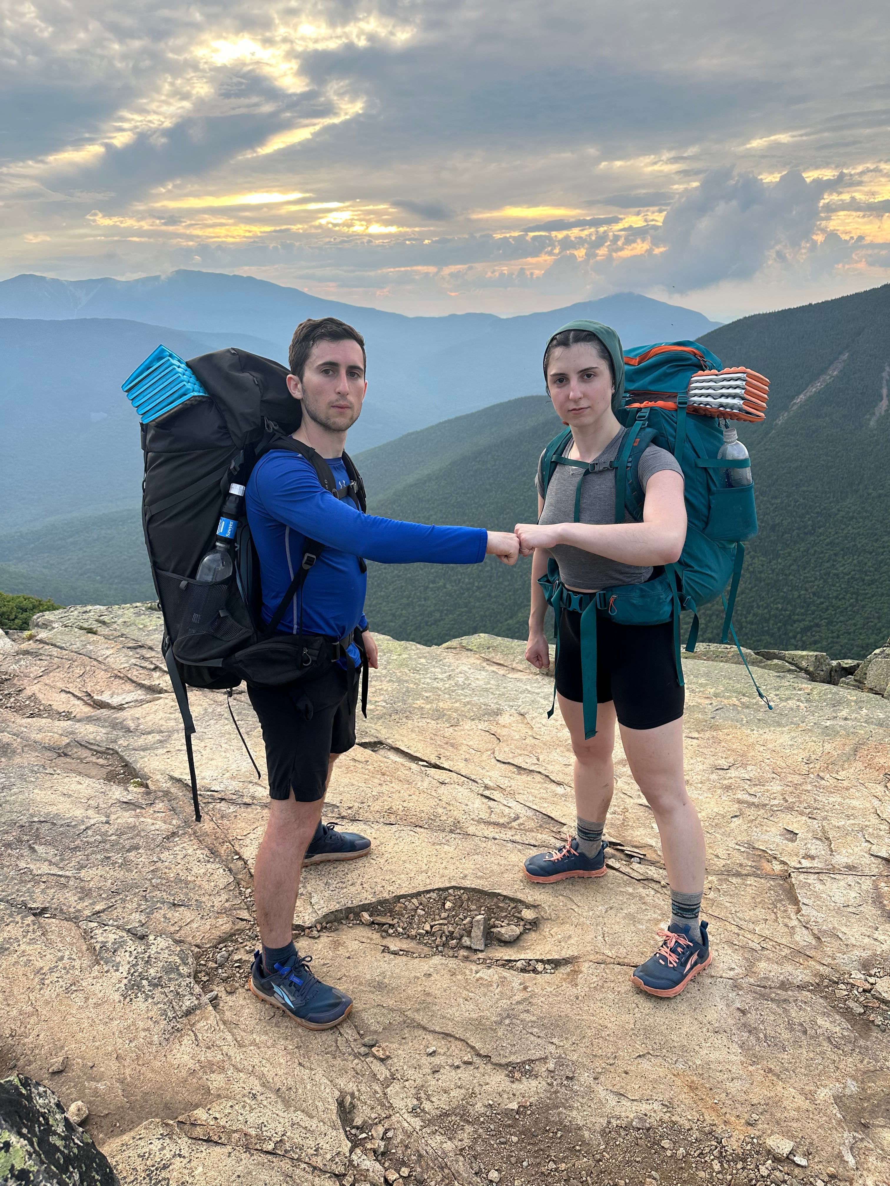 Ari and Montana fist-bumping on a summit in hiking packs